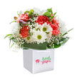 This bouquet, artfully nestled in a modern white gift bag, overflows with the joyful atmosphere of Pentonville and its spirited streets. Soft coral and rich red carnations spread exuberant colour and texture, their petals endlessly ruffled to invite a sense of comfort and abundance. White daisies, each with a lively yellow-green core, beam amidst the arrangement, while baby's breath tumbles delicately between blooms-adding a touch of innocence, like laughter drifting through Chapel Market. Deep green leaves create an embracing halo around the base, shiny and rich, evoking the gardens of nearby Barnsbury. Peeking purple buds on the left suggest hope and anticipation, the promise of continued beauty. Every flower is placed with intention, producing a rounded, generous structure that seems to glow against the spotless white of the background. Whether destined for a birthday, a congratulatory surprise, or an everyday act of kindness, this bouquet is primed for delivery throughout Pentonville-a fresh reminder of how flowers can brighten every neighbourhood moment and connection.